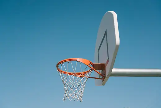 Basketballkorb mit orangem Ring und weißem Netz vor blauem Himmel
