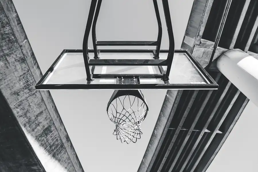 Basketballkorb von unten fotografiert, dahinter die Betondecke des Freiplatzes und heller Himmel