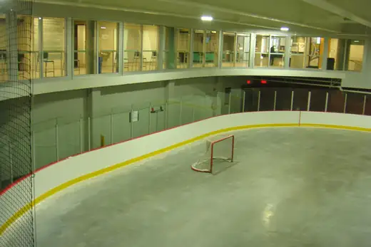 Eishockeytor auf der leeren Eisfläche, dahinter die Bande und die Fenster der Halle