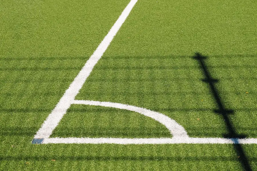 Eckpunkt eines Fußballplatzes: weiße Viertelkreislinie auf grünem Kunstrasen