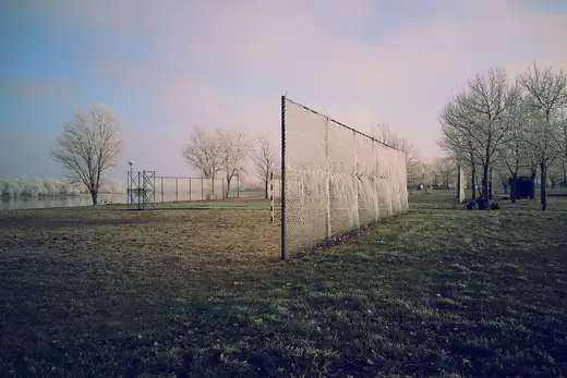 Fußballplatz im Nebel hinter einem Ballfangnetz, dahinter kahle Bäume