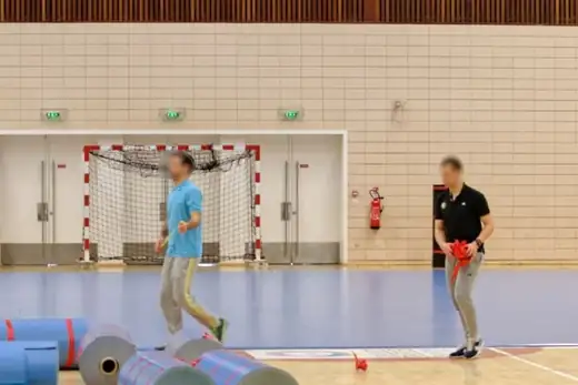Handballtor in einer Halle mit hellem Parkettboden, davor aufgerollte blaue Bodenmatten